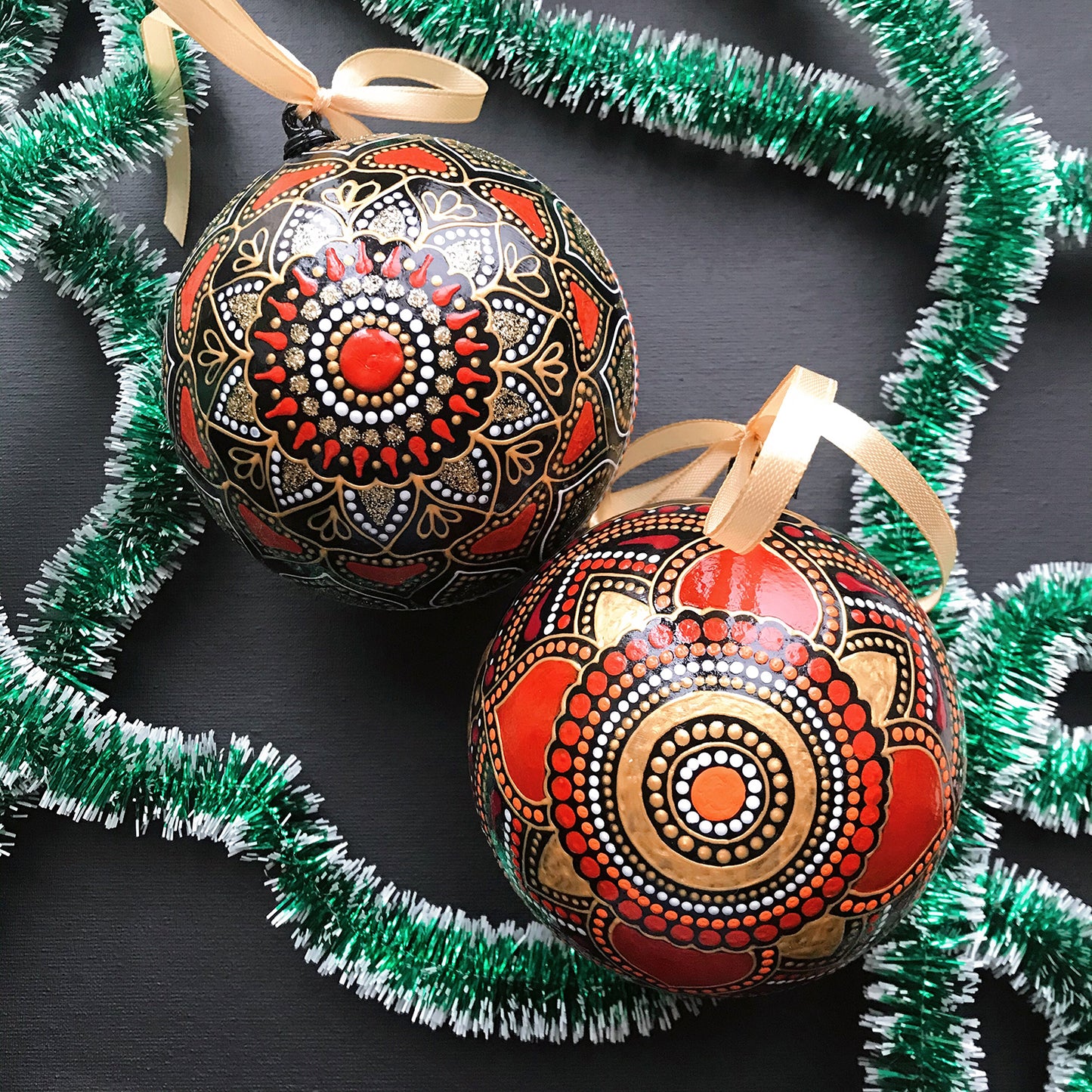 Two red Christmas ornaments with hand-painted mandala design. Black background, view from the top.
