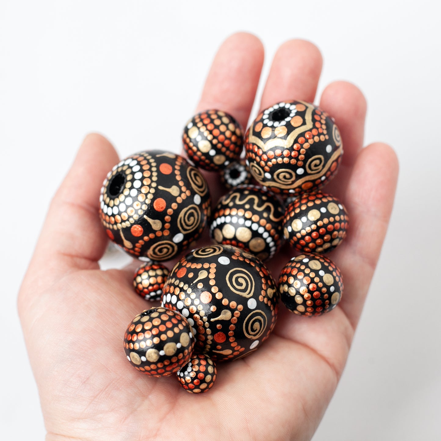 Wooden beads in a hand, different sizes. Hand-painted beads in african style, gold and copper colors.