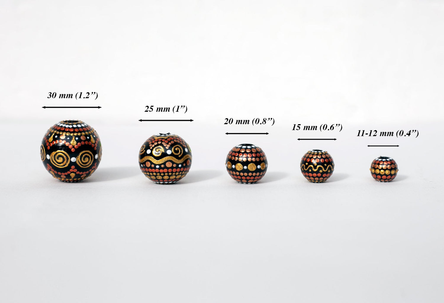 Wooden round beads in a row to show different sizes. Hand-painted beads in african style, gold and copper colors.