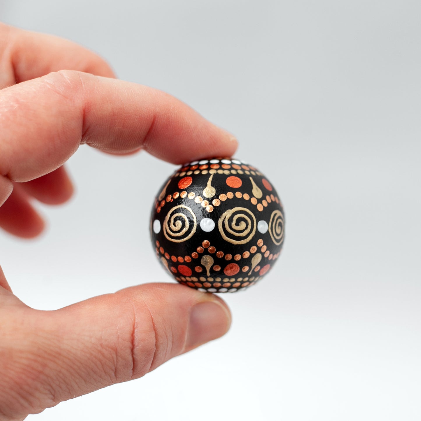 Large round bead, close-up view holding in fingers. Hand-painted wooden bead in african style, gold and copper colors.