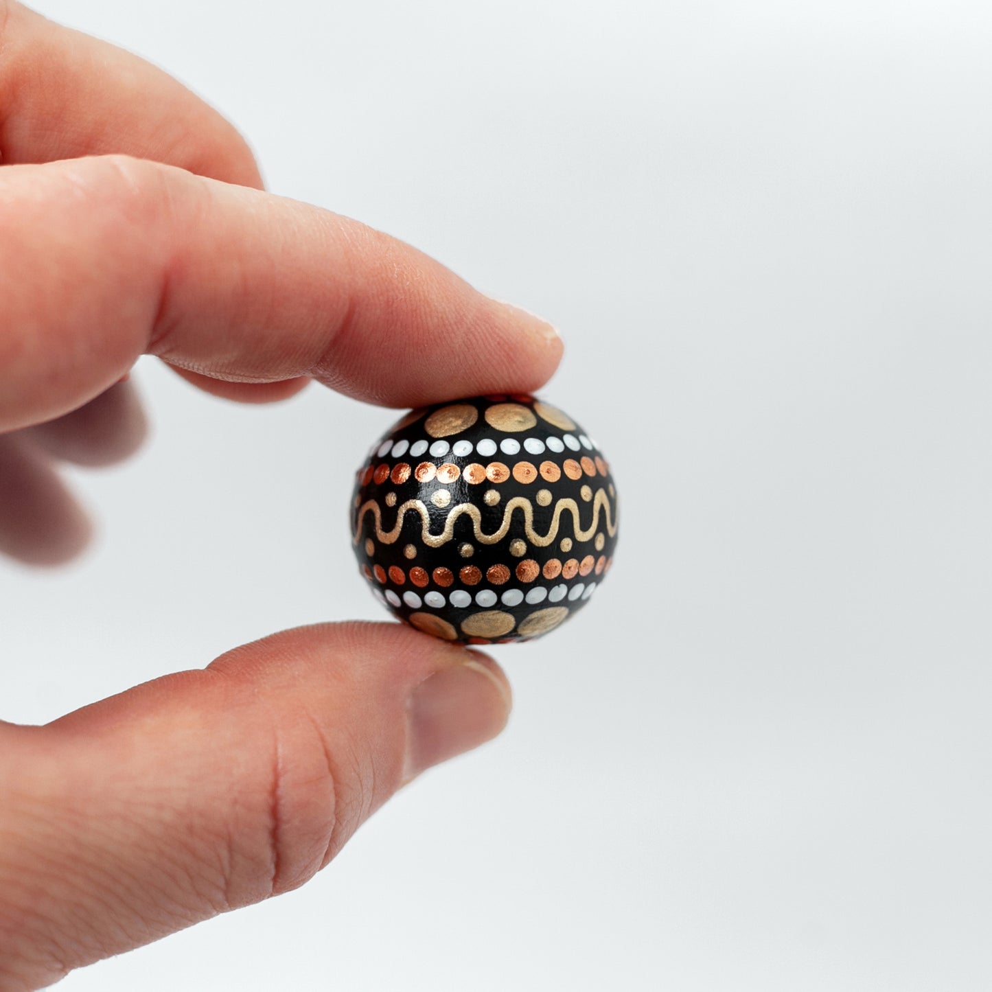 Large round bead, close-up view holding in fingers. Hand-painted wooden bead in african style, gold and copper colors.