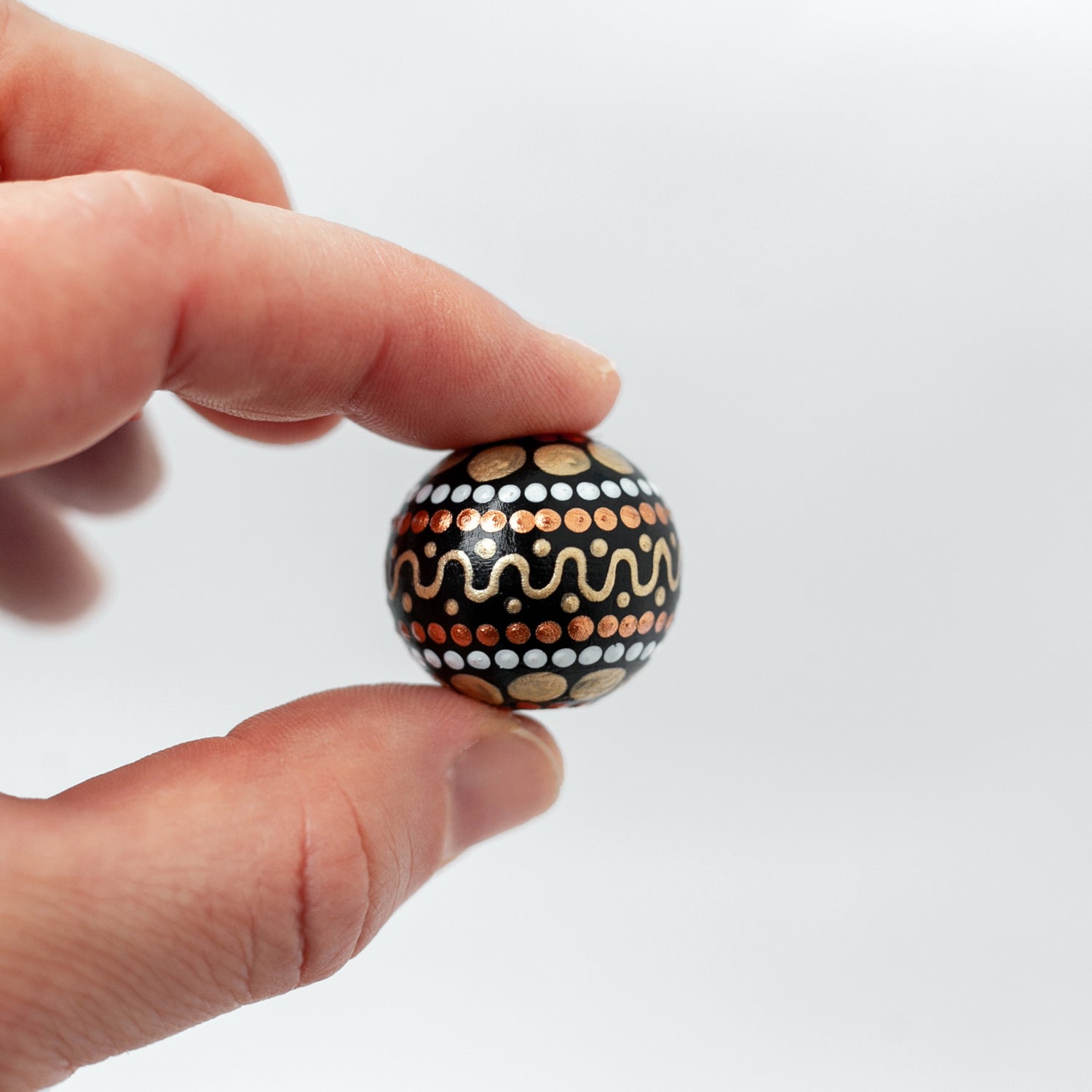 Large round bead, close-up view holding in fingers. Hand-painted wooden bead in african style, gold and copper colors.