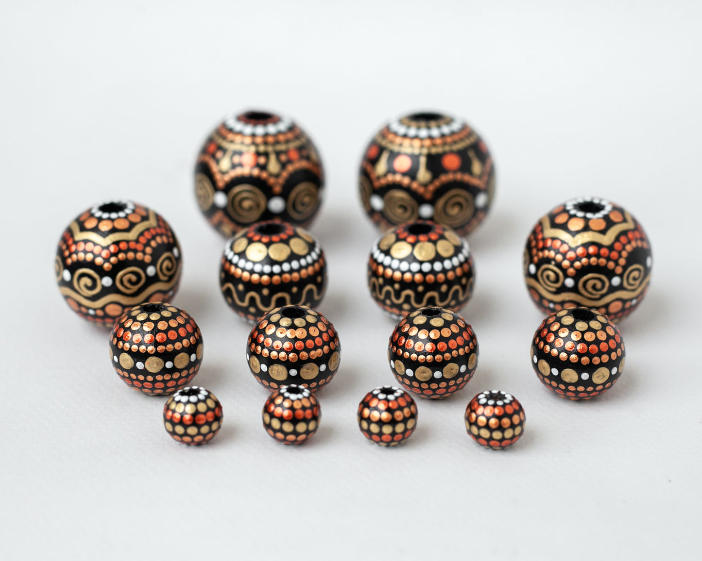Wooden round beads in a row to show different sizes. Hand-painted beads in african style, gold and copper colors.