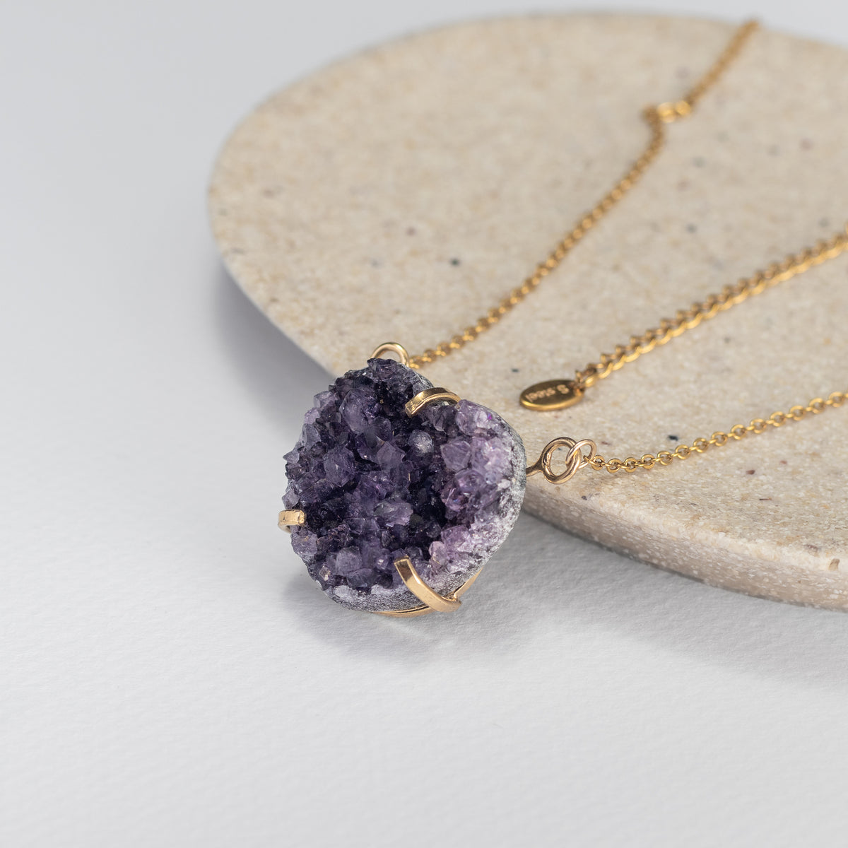 amethyst druzy heart necklace with a gold chain on a stone plate