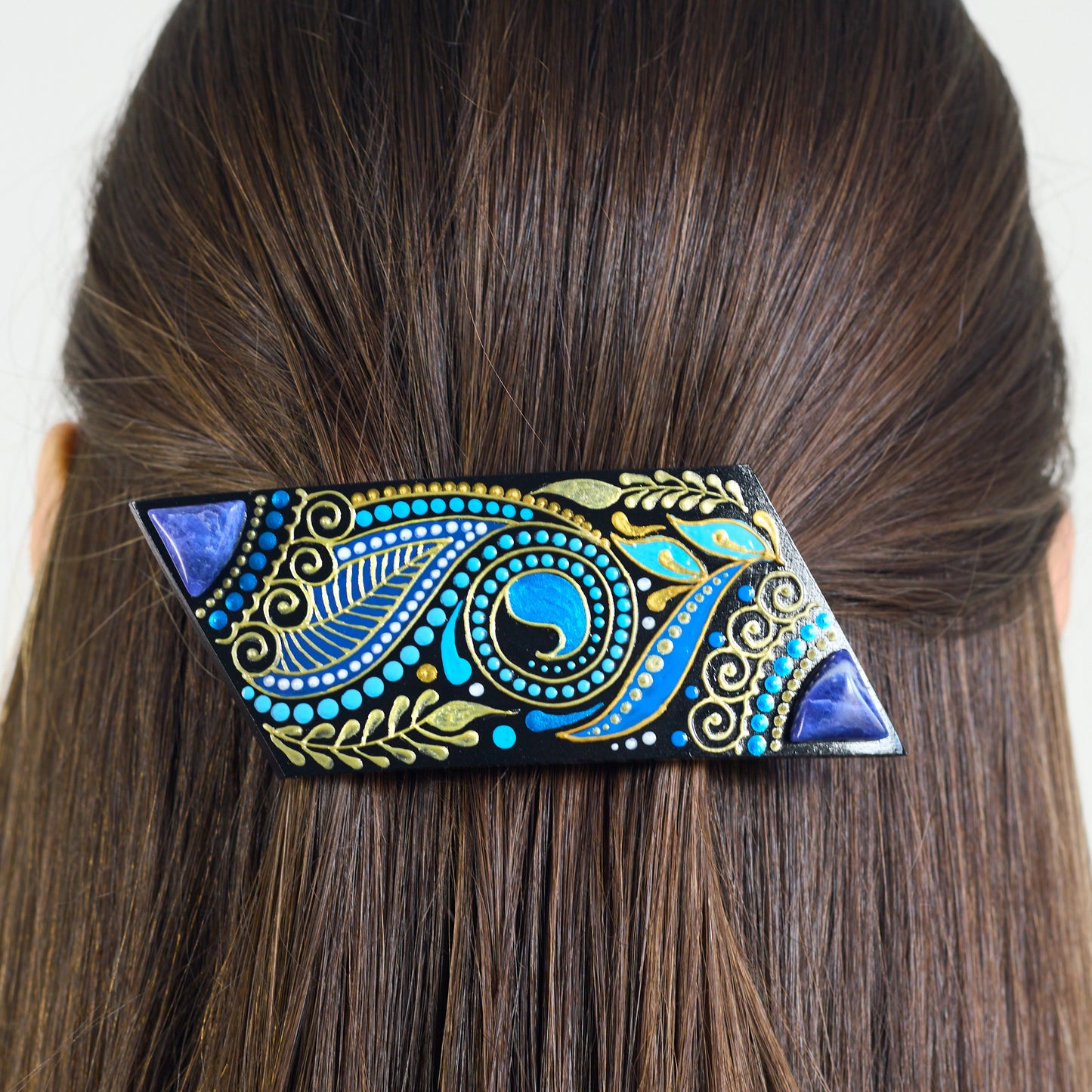Decorative hair clip with blue and gold patterns on brown hair against a white background
