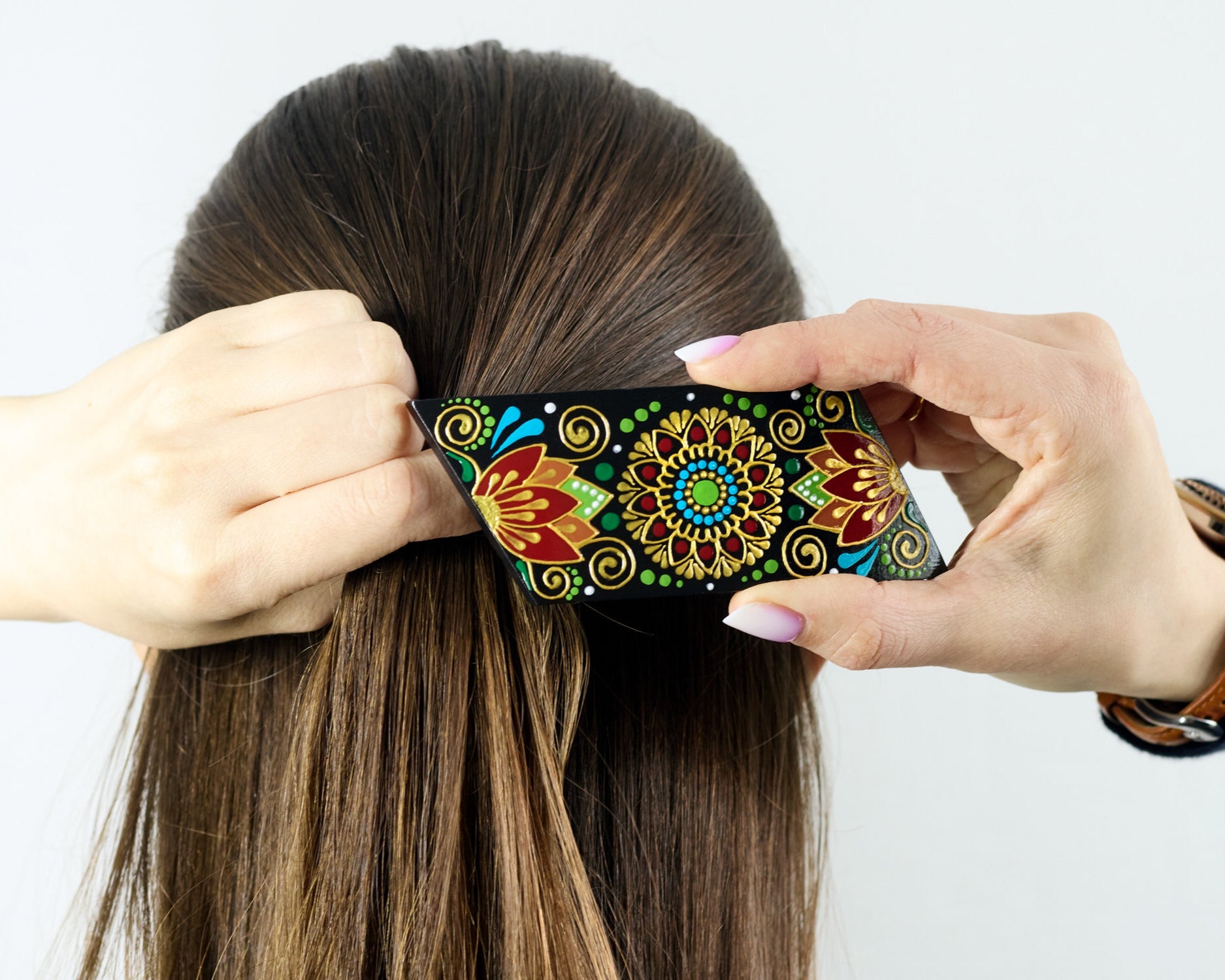 A woman fastens a hair clip hand-painted with floral design at the back of her dark hair.