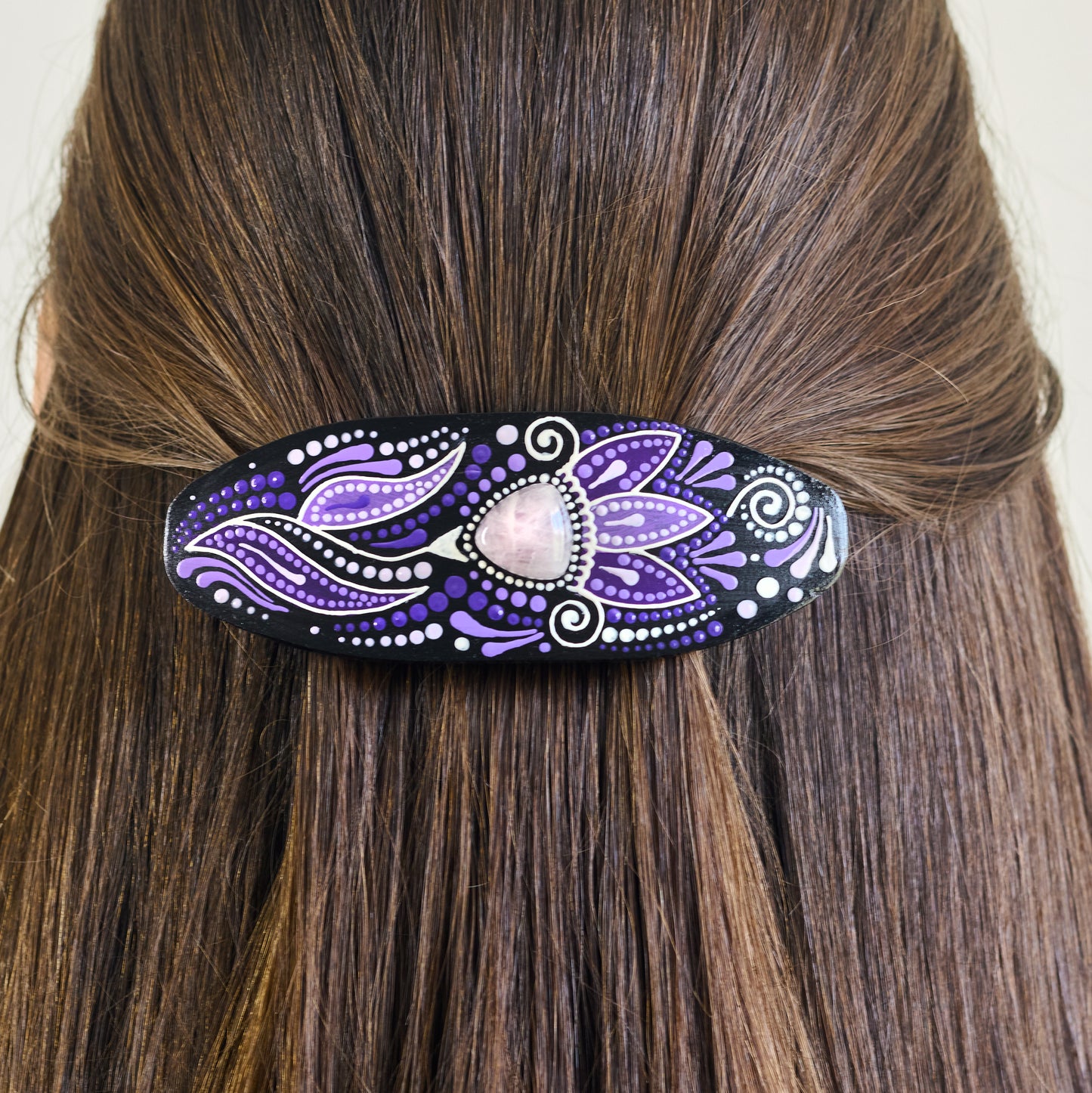 Close-up of dark hair with a purple hand-painted wooden barrette clipped in.