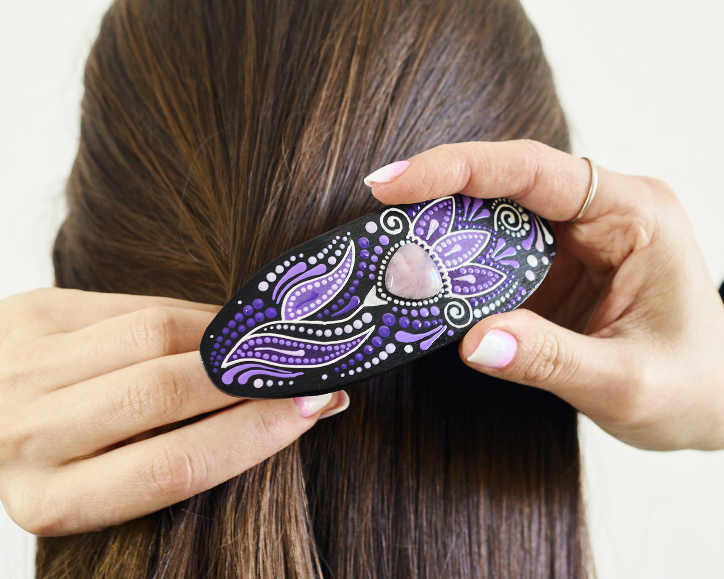 Women's hands clipping on her dark hair wooden barrette with a floral hand-painted design.