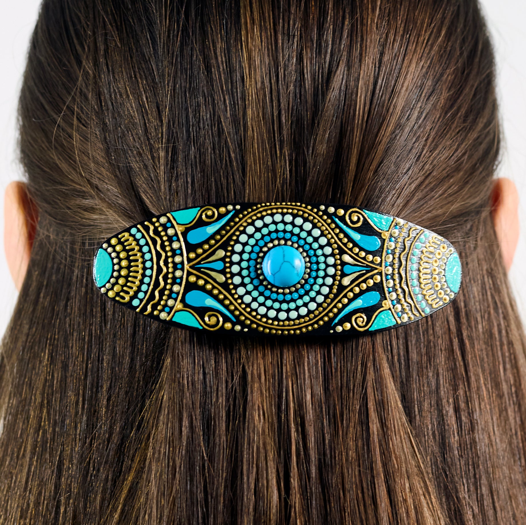Close-up of dark hair with a colorful hand-painted wooden barrette clipped in, turquoise blue design.