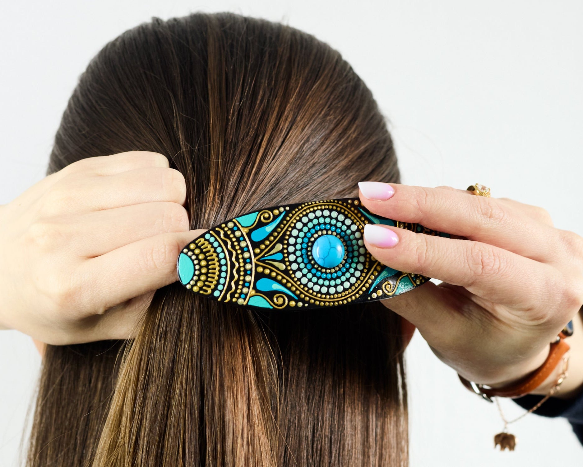 Close-up of dark hair with a colorful hand-painted wooden barrette clipped in, turquoise blue design, women's hand holding it.