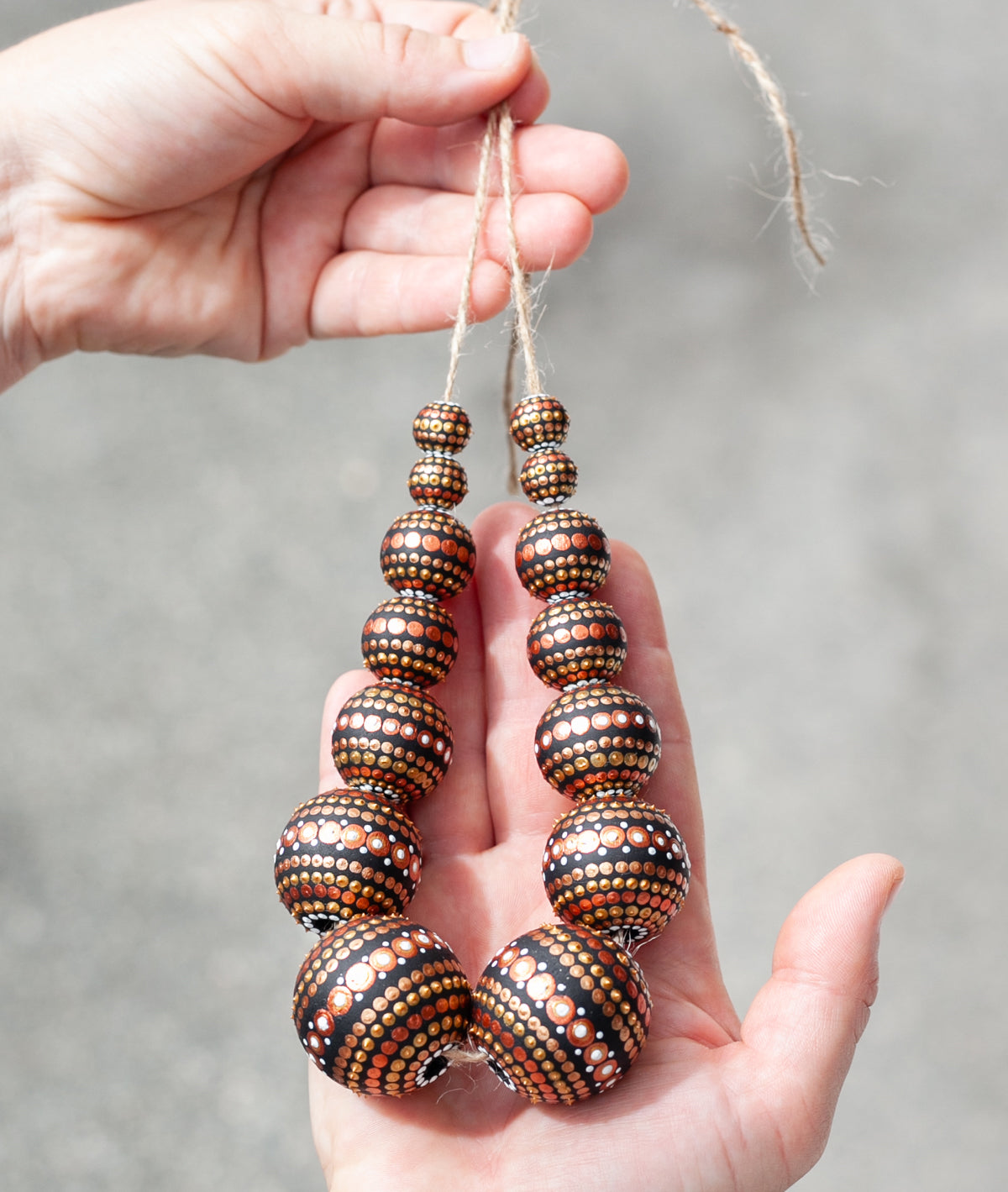 Wooden round beads collected in a garland, holding in hands. Hand-painted beads in african style, gold and copper colors.