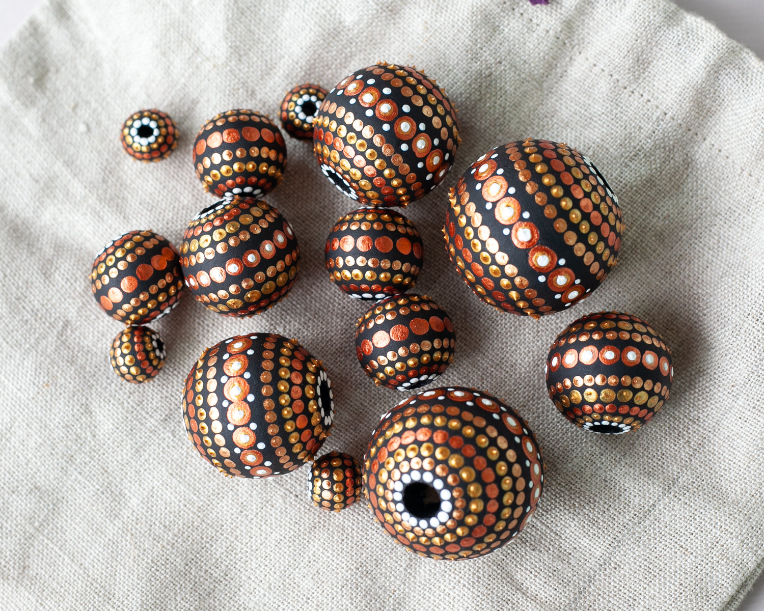 Large and small round  beads spread on the linen bag, wooden hand-painted beads in african style. Gold and copper colors, view from the top