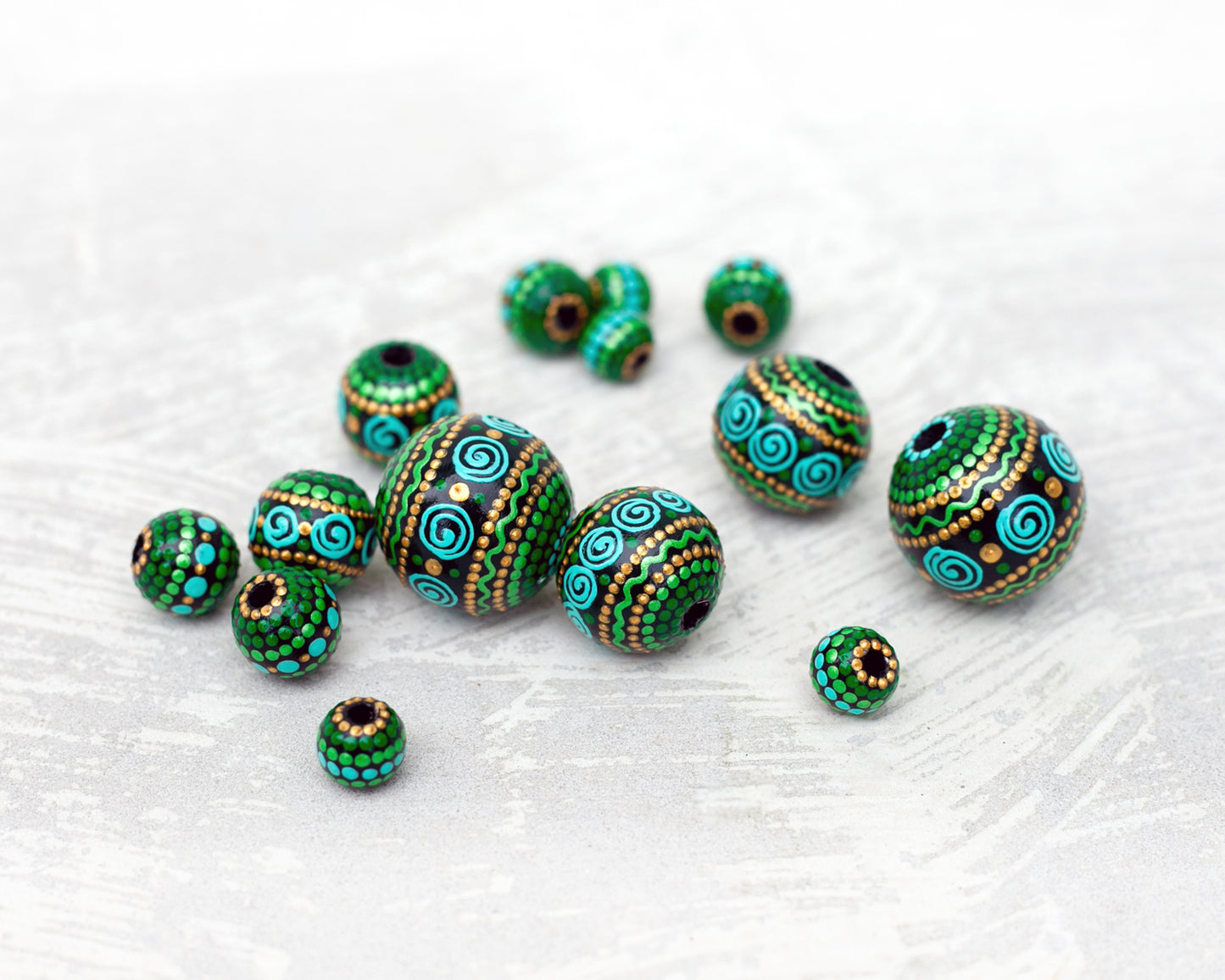 Large and small round  beads spread on the table, wooden hand-painted beads in african style. Green, mint and gold colors, close-up view