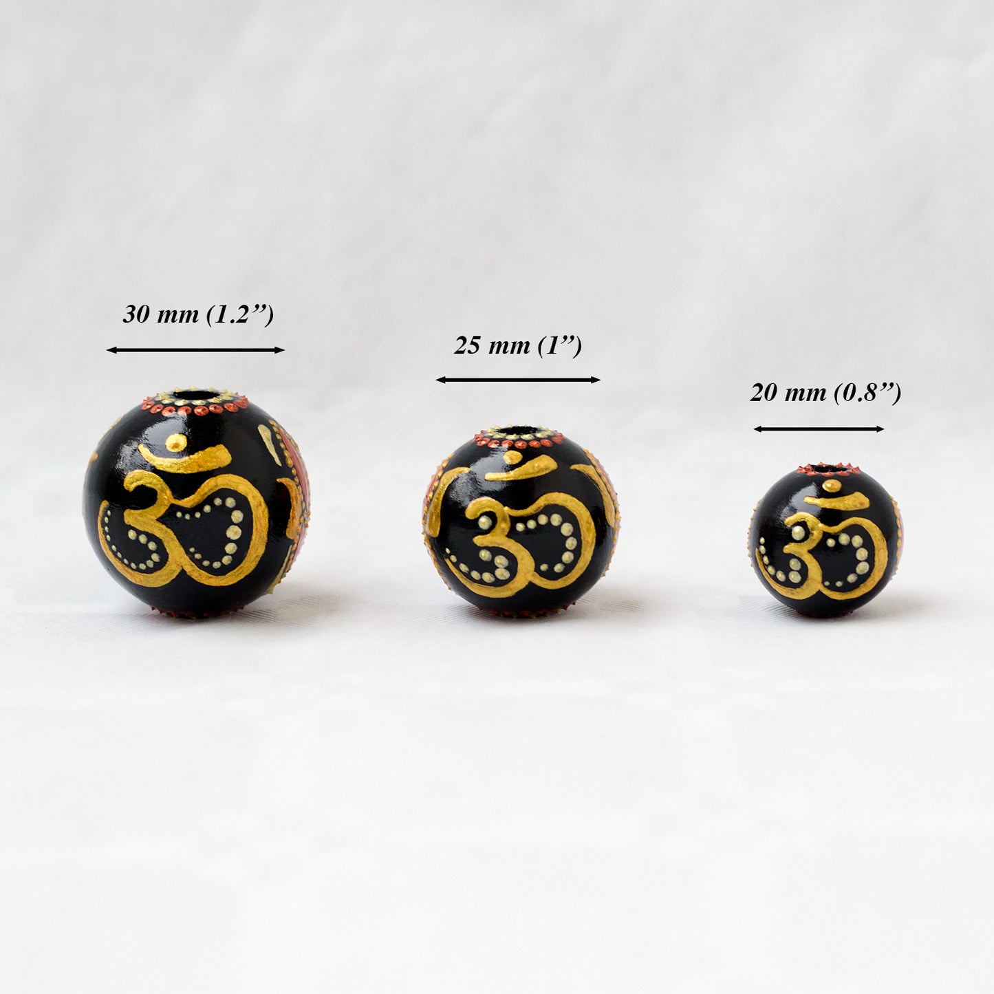 Wooden round beads in a row to show different sizes. Hand-painted large beads with the Om symbol.