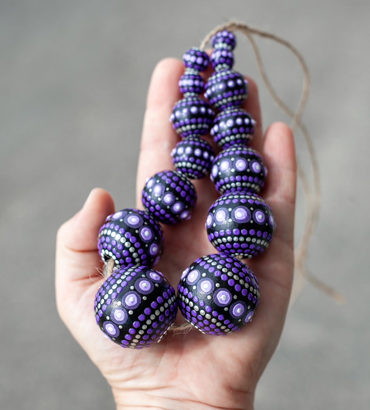 Wooden round beads collected in a garland, holding in hands. Hand-painted purple beads in african style.