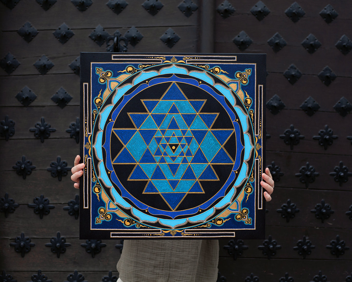 Sri Yantra painting in blue and gold colors. Artist holding the canvas in hands to show dimensions. 40x40 cm (16×16 inches) size.