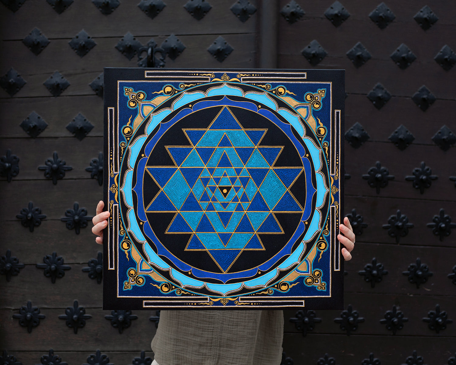 Sri Yantra painting in blue and gold colors. Artist holding the canvas in hands to show dimensions. 40x40 cm (16×16 inches) size.