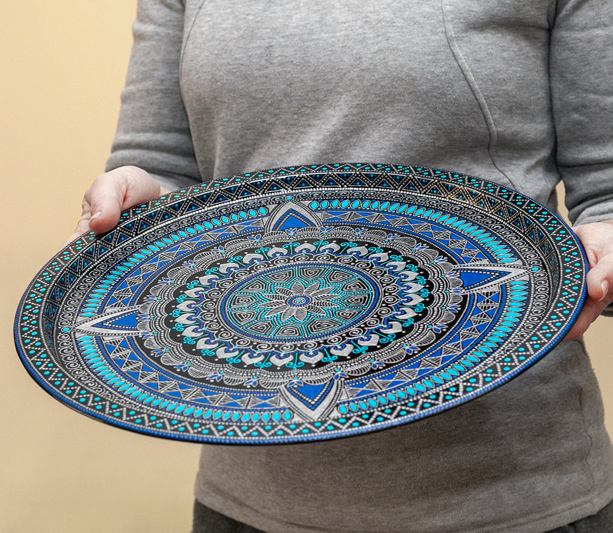 Woman holds in hands blue round metal serving tray from Moroccan collection made in blue.