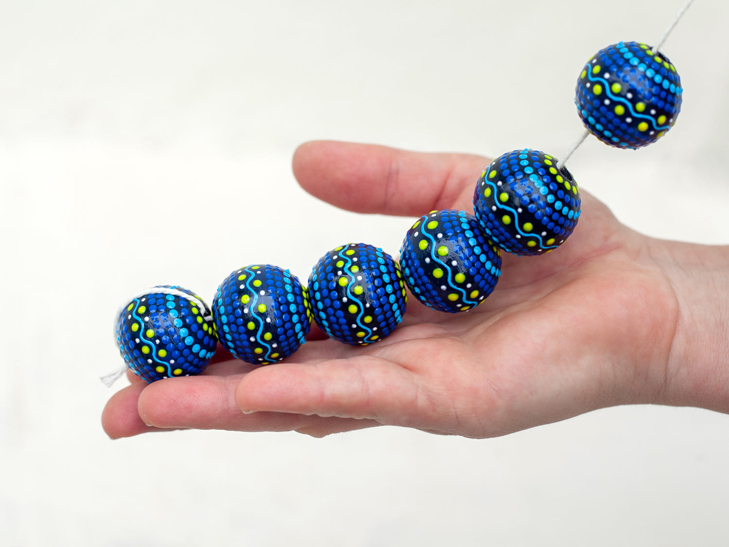Wooden round beads collected in a garland, holding in a hand. Hand-painted wooden beads in scandinavian style, blue and yellow colors.