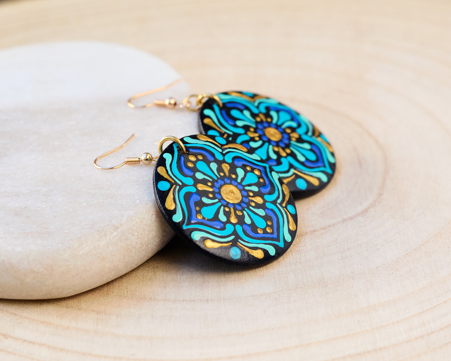 Colorful mandala-patterned earrings on a wooden surface with stones.