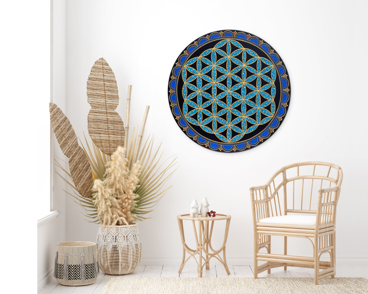 Flower of Life painted on a round canvas board, blue colors. Painting is hanging on a wall in a boho room, rattan chair and large vases on the floor.