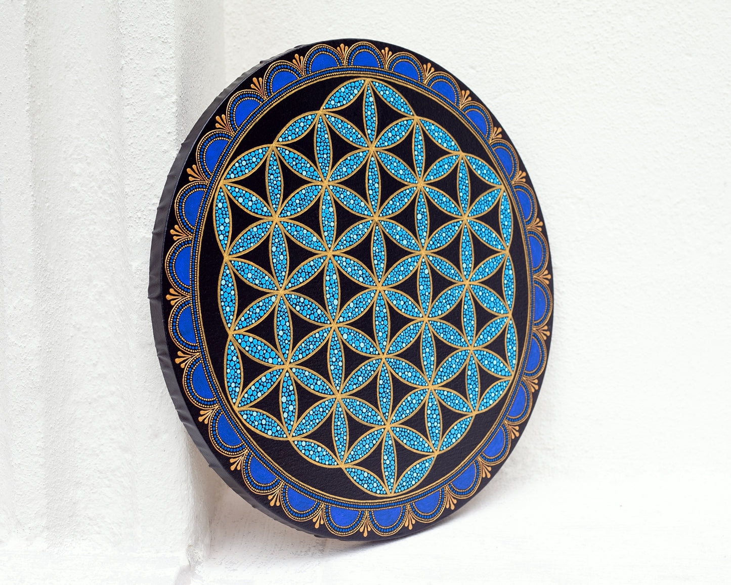 Flower of Life painted on a round canvas board, dot art technique, blue colors. Side view on a white background.