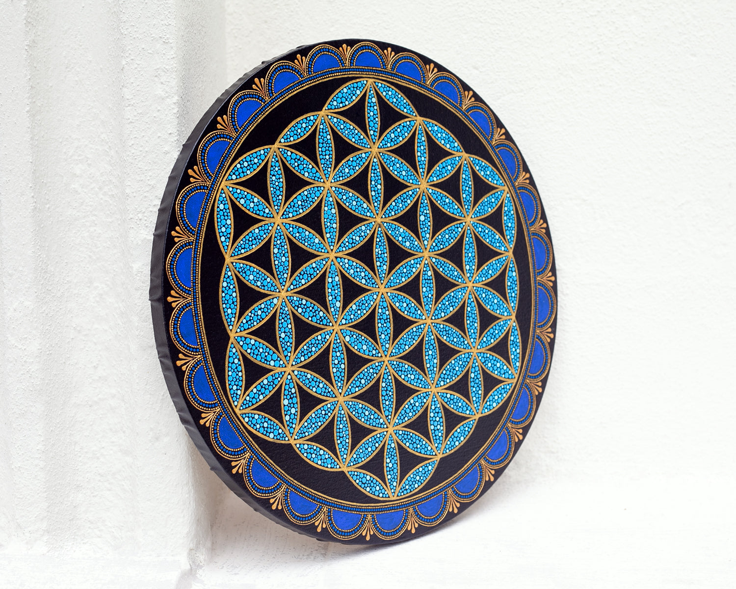Flower of Life painted on a round canvas board, dot art technique, blue colors. Side view on a white background.