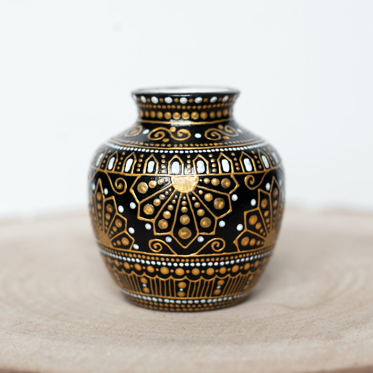 A small, hand-painted ceramic bud vase with greek style gold patterns, sitting on a wooden slab.