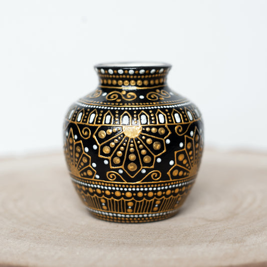 A small, hand-painted ceramic bud vase with greek style gold patterns, sitting on a wooden slab.