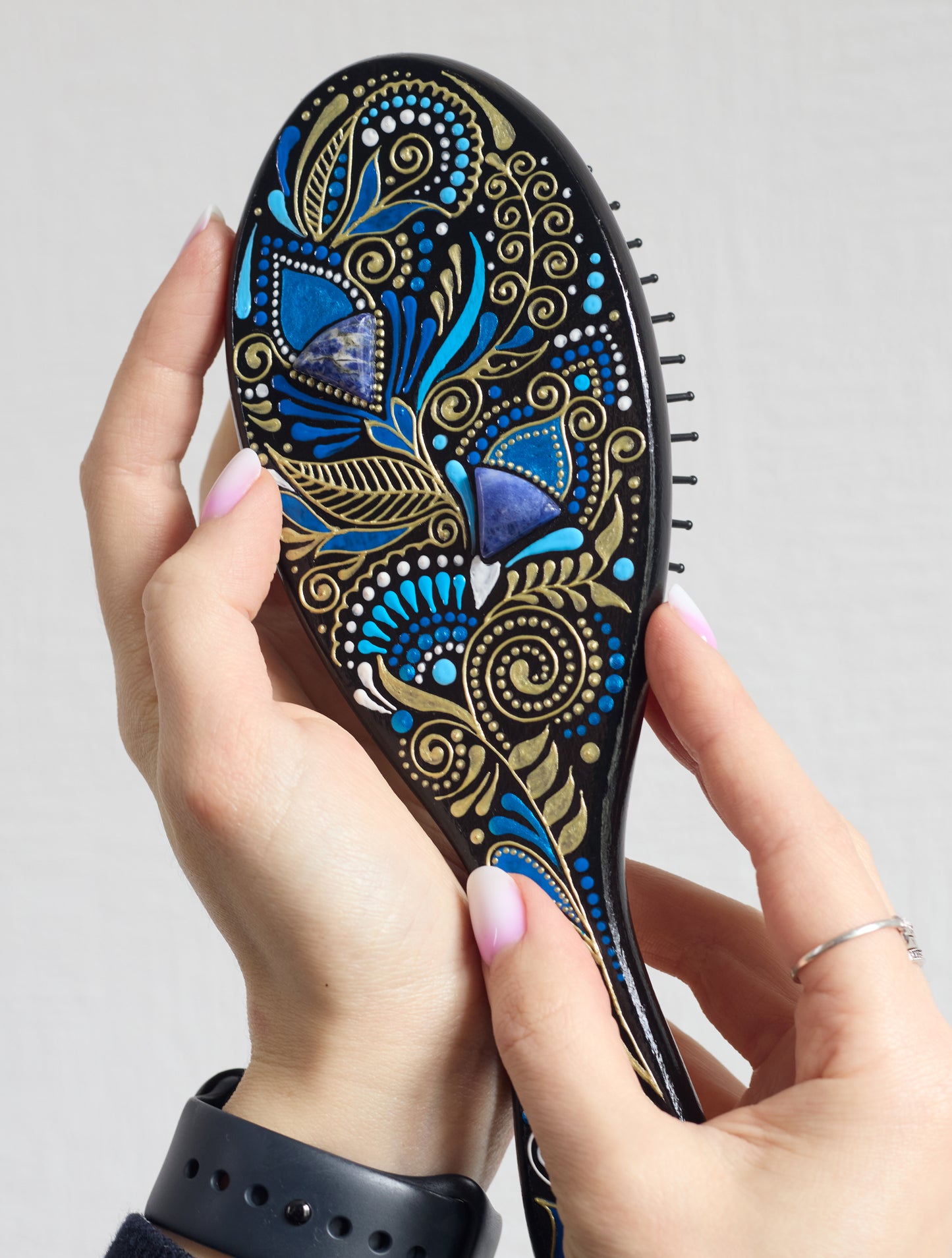 Hand holding a hand-painted wooden paddle hairbrush with blue floral design.