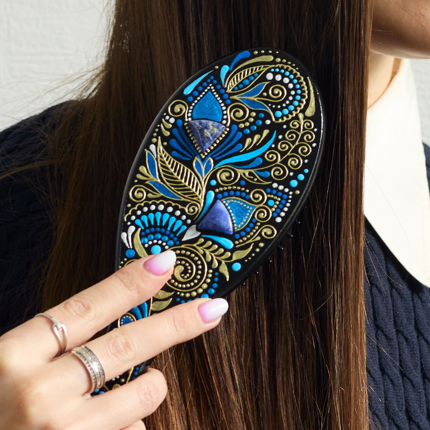 Close-up of a hand brushing dark hair with a hand-painted wooden hairbrush, focusing on the brush in use.
