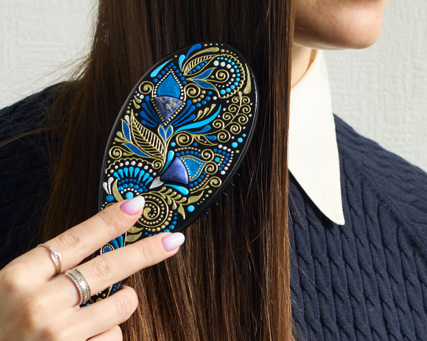 Close-up of a hand brushing dark hair with a hand-painted wooden hairbrush, focusing on the brush in use.