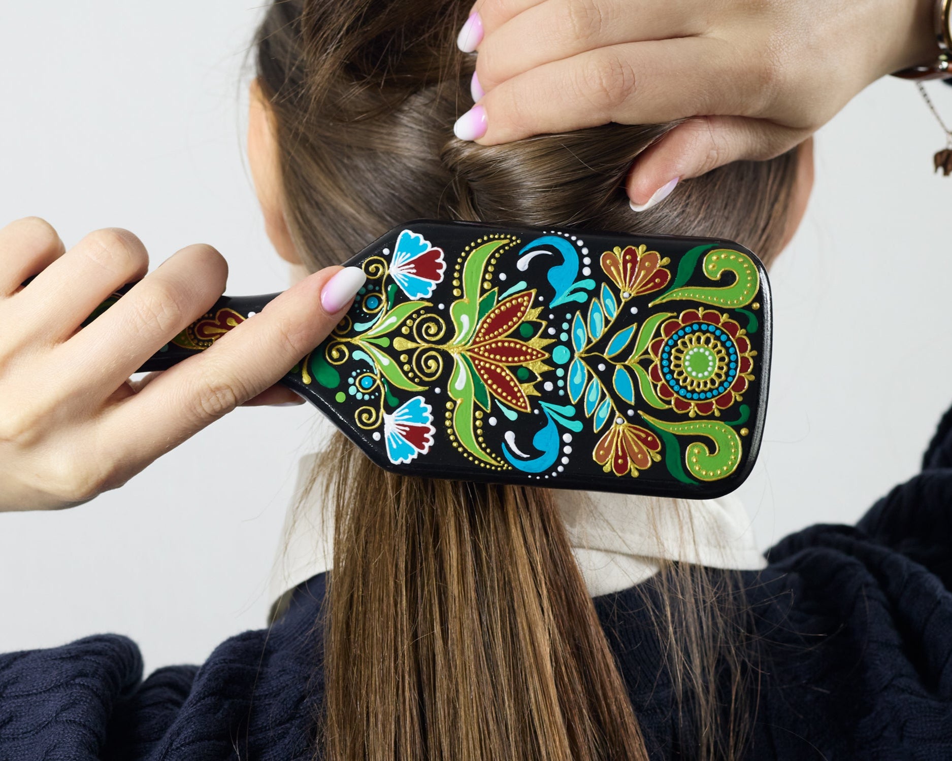 Close-up of a hand brushing dark hair with a hand-painted wooden hairbrush, focusing on the brush in use.