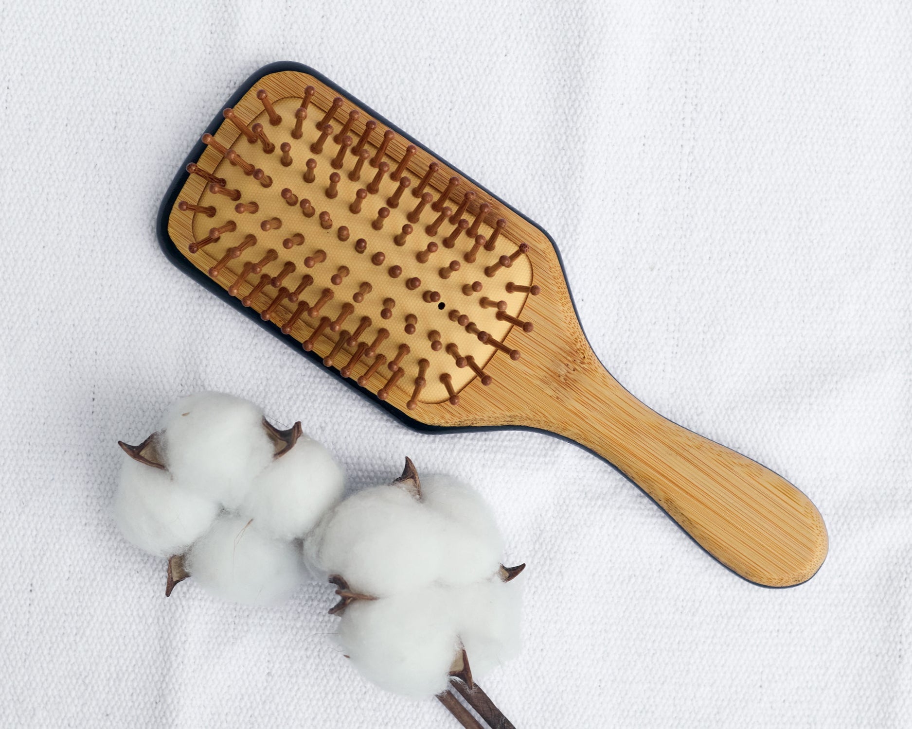 Top view of a wooden paddle hairbrush showing the back side with natural wooden bristles, placed on a light surface.