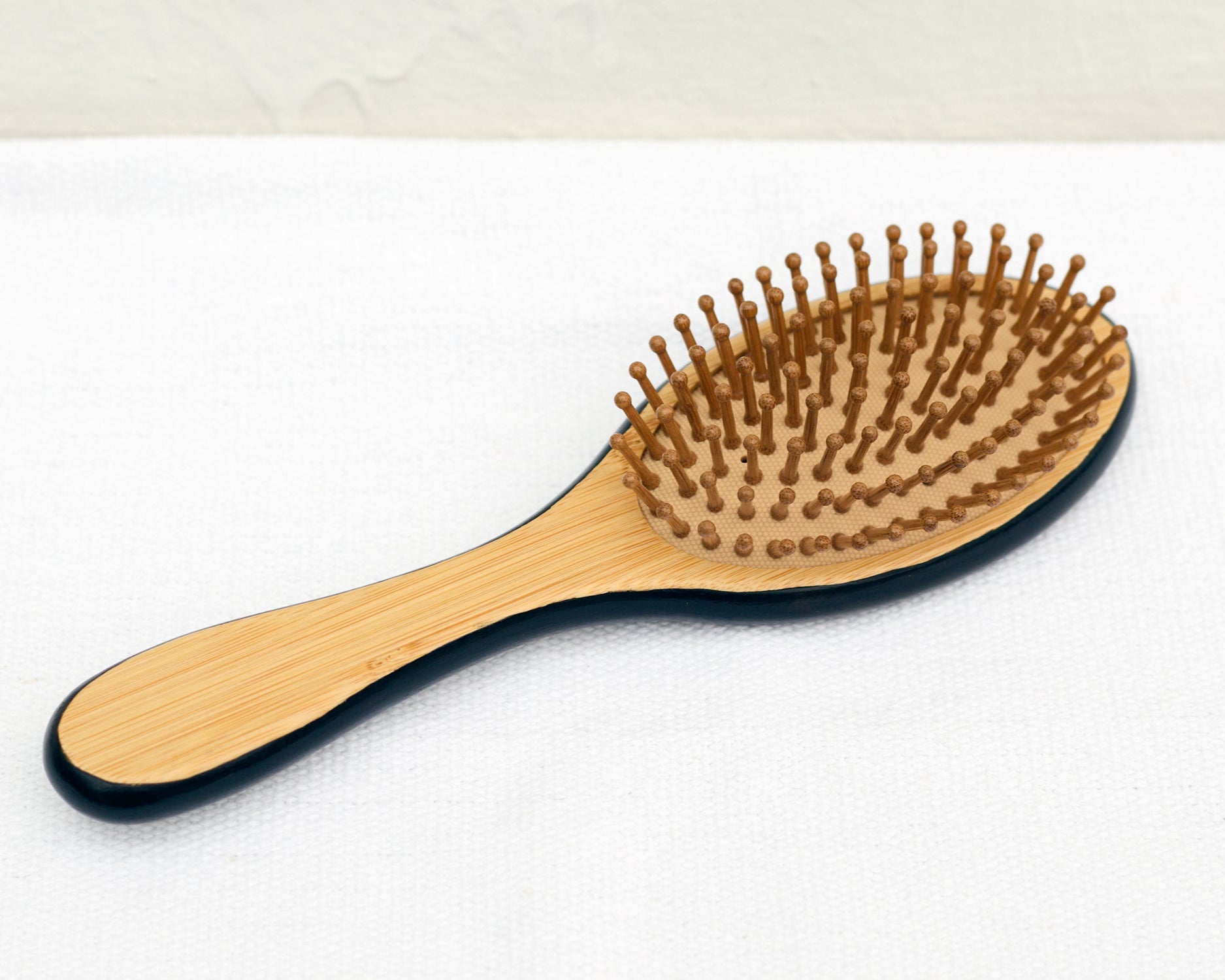 Top view of a wooden paddle hairbrush showing the back side with natural wooden bristles, placed on a light surface.