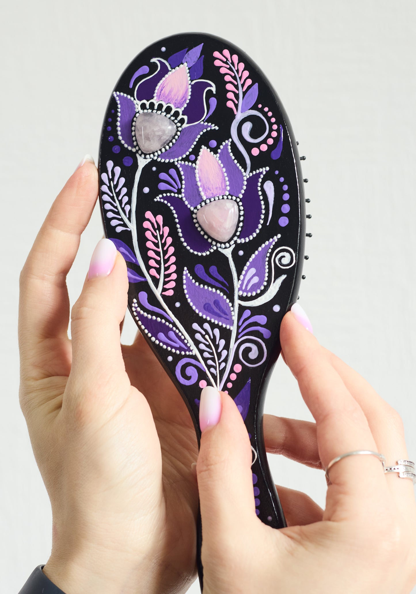 Hand holding a purple hand-painted wooden paddle hairbrush with floral design.