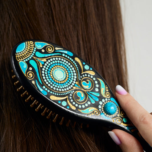 Close-up of a hand brushing dark hair with a hand-painted wooden hairbrush, focusing on the brush in use.