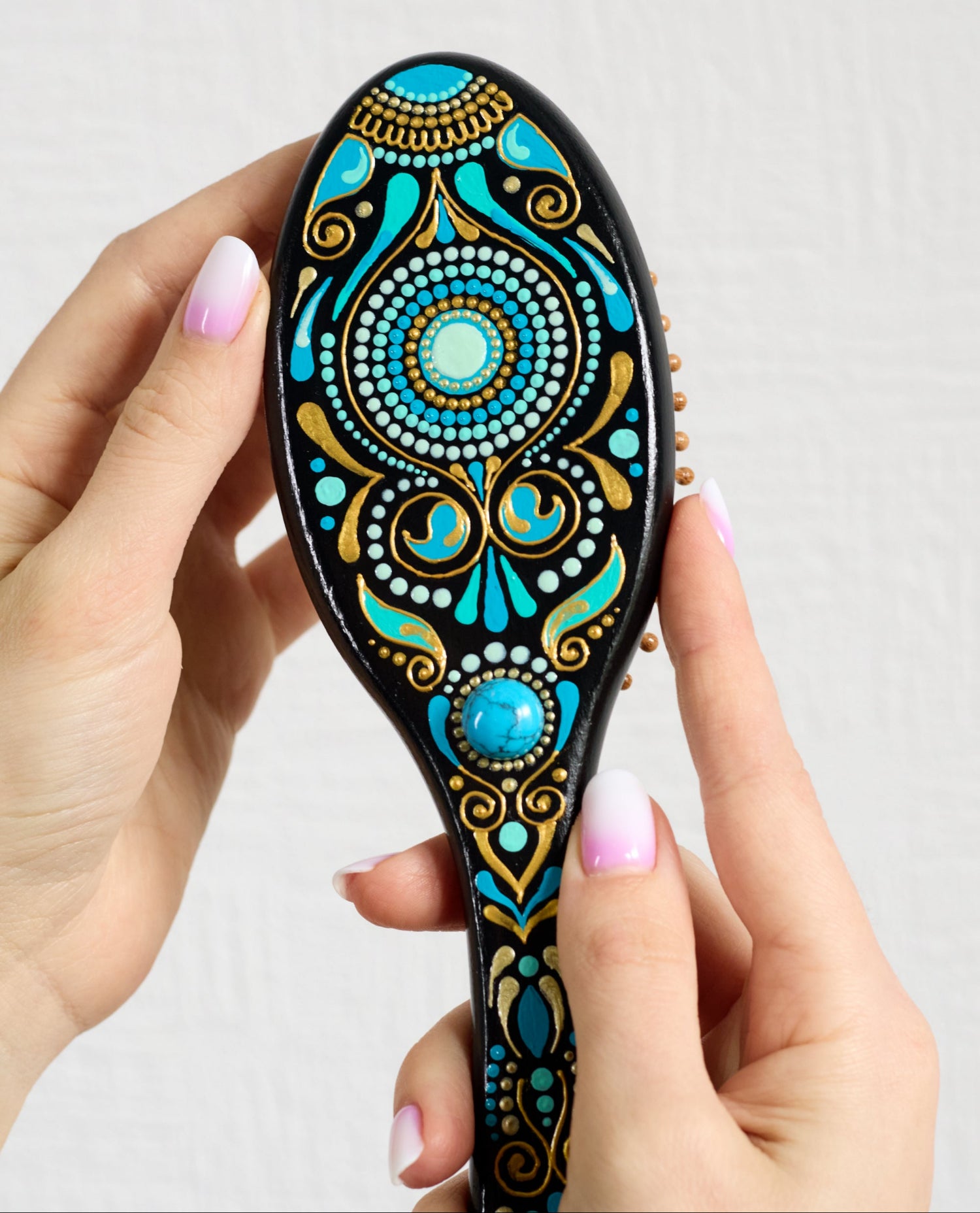 Hand holding a colorful hand-painted wooden paddle hairbrush with turkish  design in turquoise blue and gold.