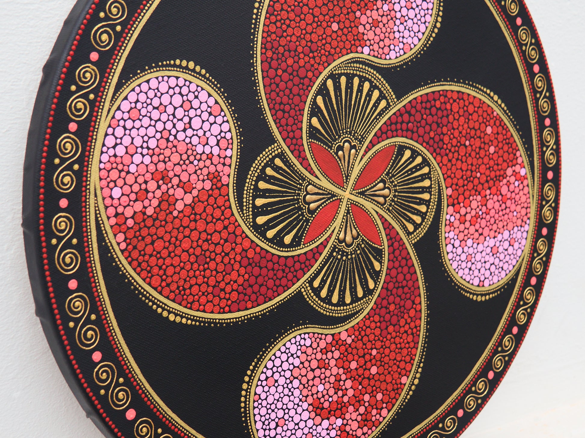 Round Lauburu Basque cross painting in pointillism, red and gold toones, detailed close-up view.