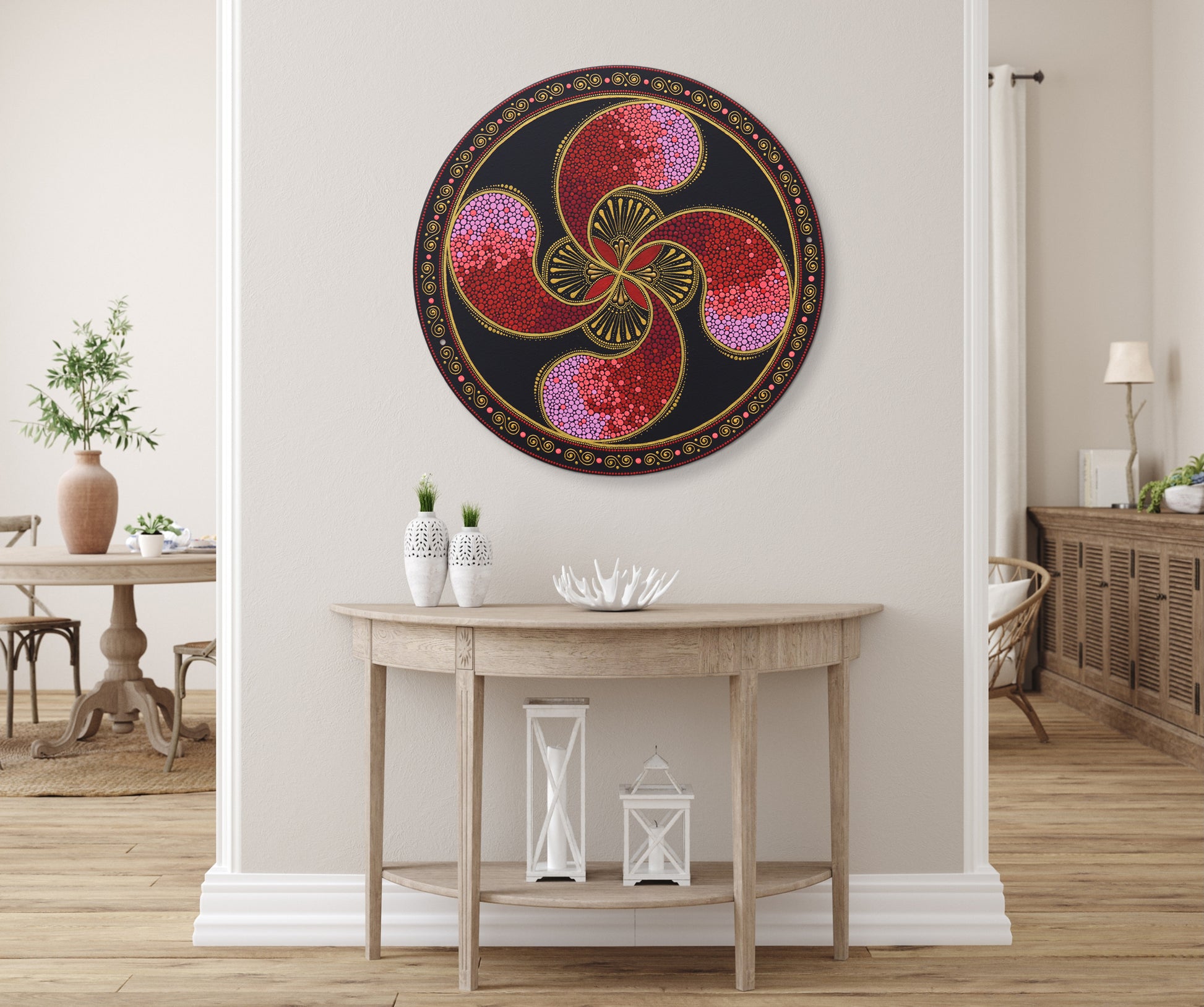Round red Lauburu pointillism painting displayed on a light wall above wooden furniture in a cozy, bohemian-style living room.