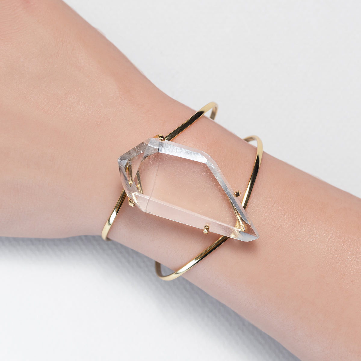 Gold bracelet with a clear crystal on a wrist against a light background