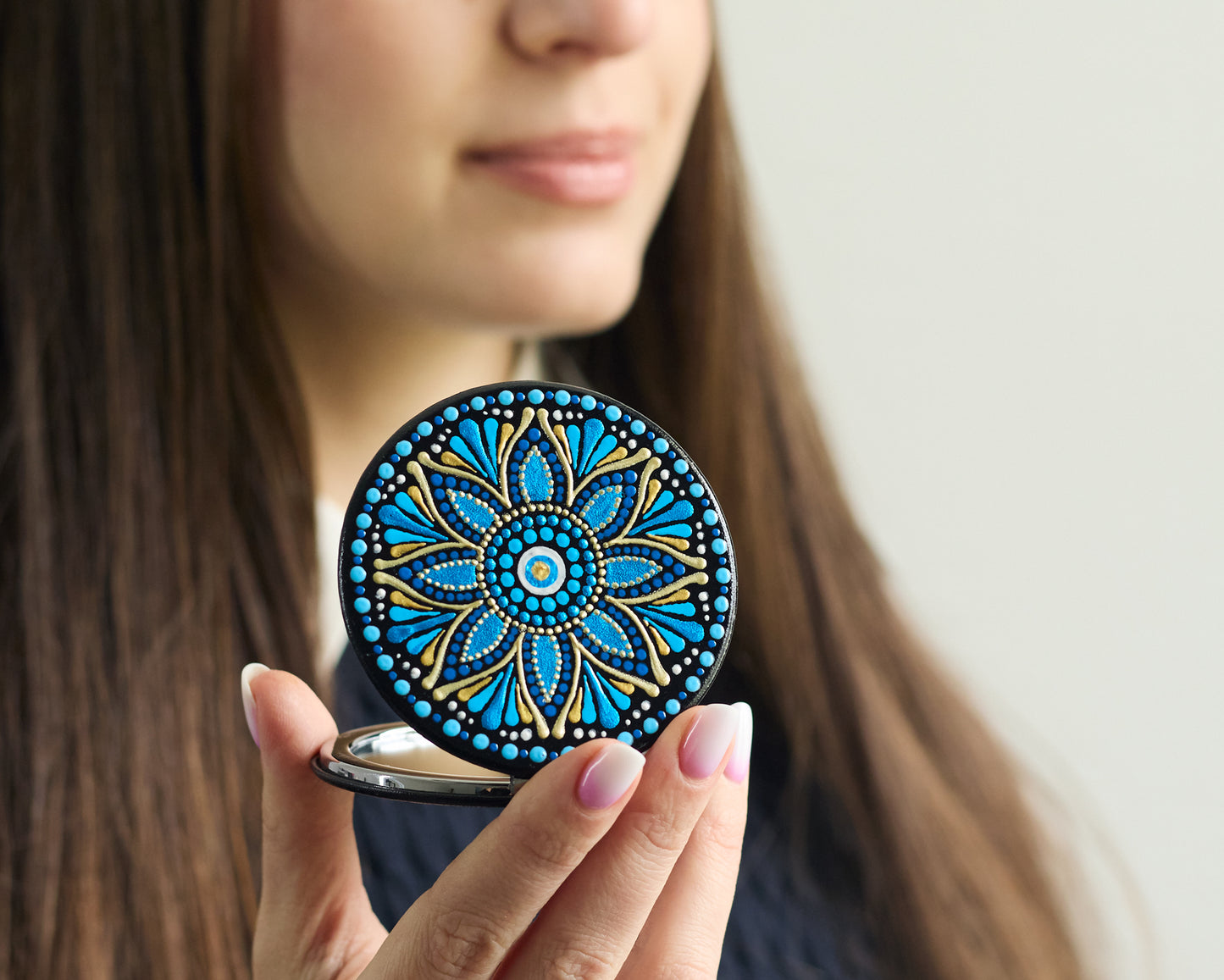 Woman looking in the compact mirror with blue mandala hand-painted design.