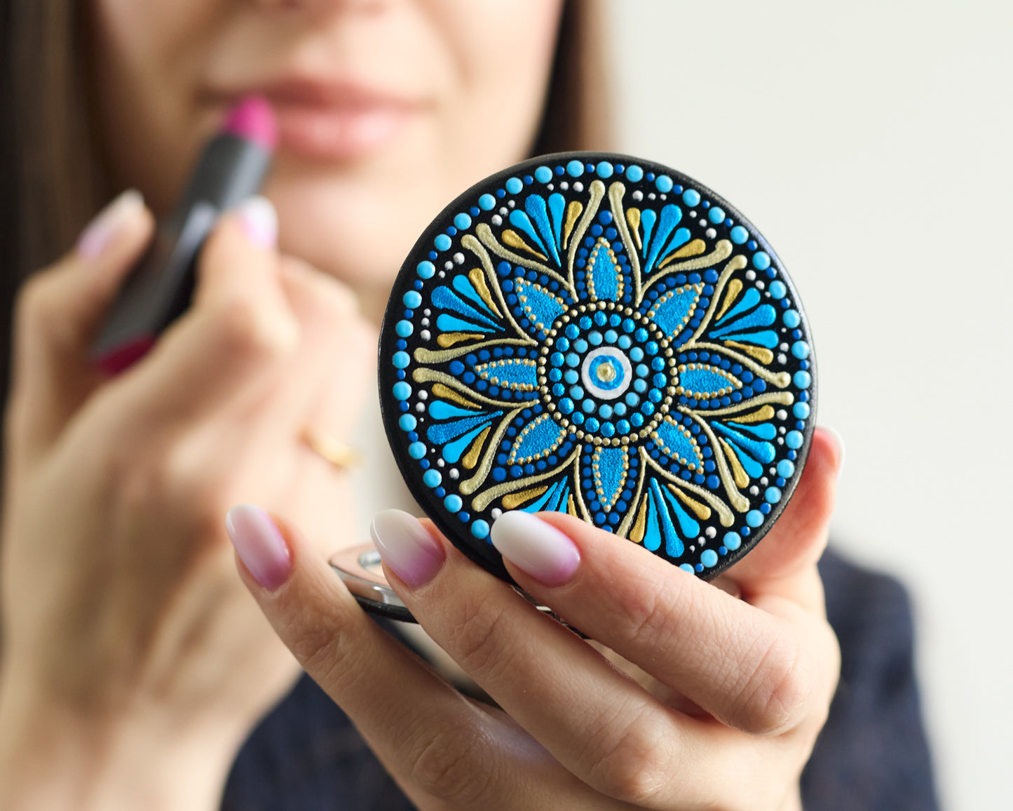 Woman making makeup looking in the compact mirror with blue mandala hand-painted design.