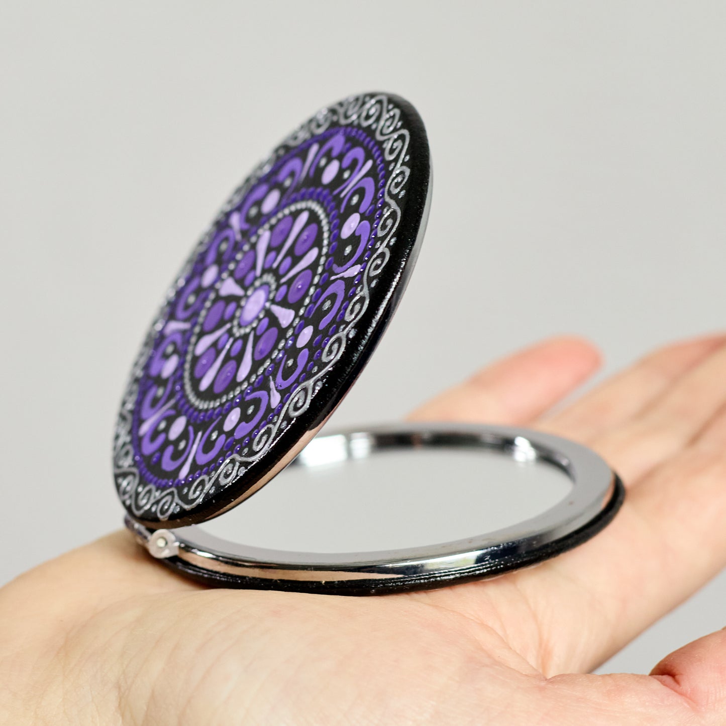 Compact mirror with purple mandala design held in a hand, round shape