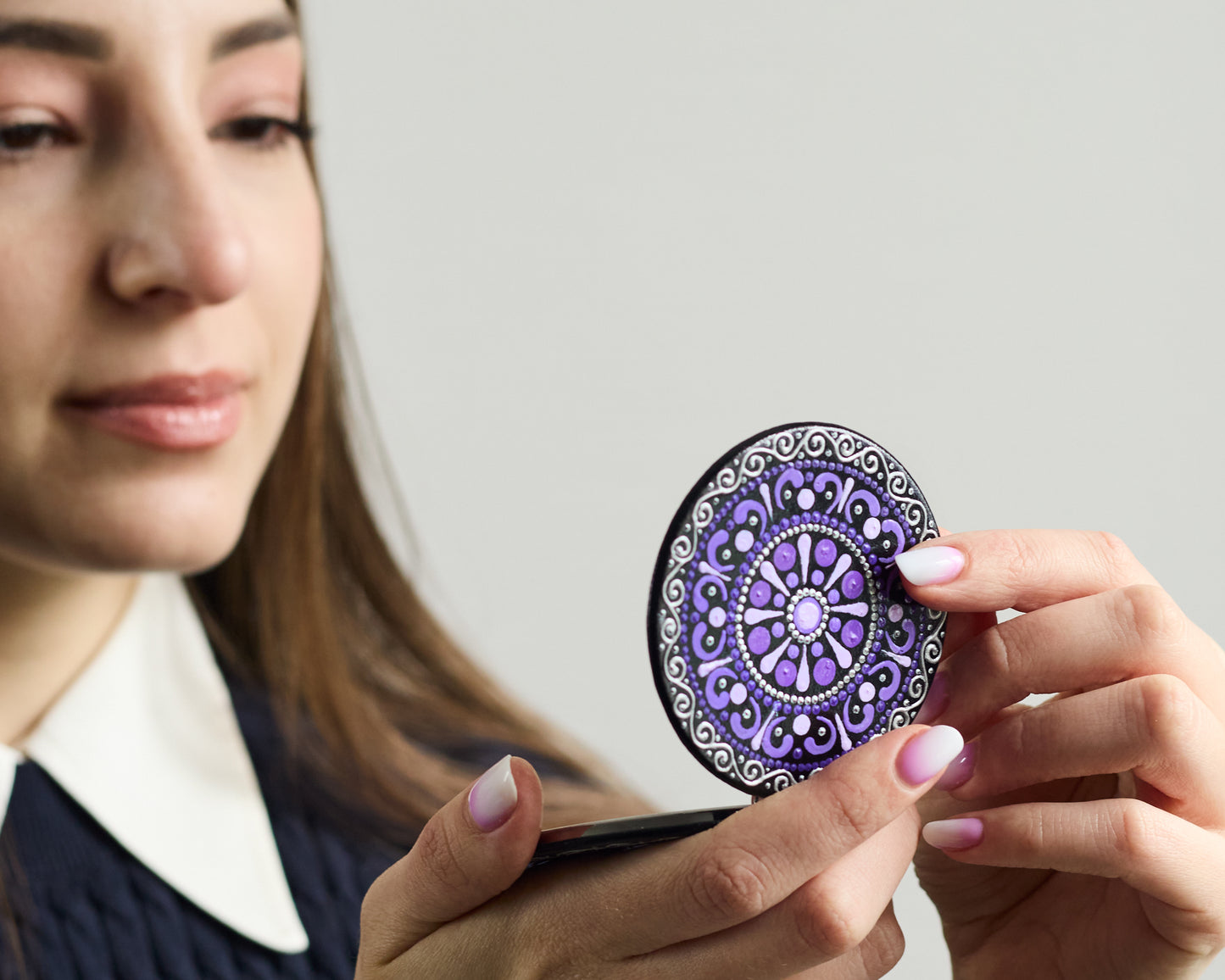 Woman looking in the compact mirror with purple mandala hand-painted design.