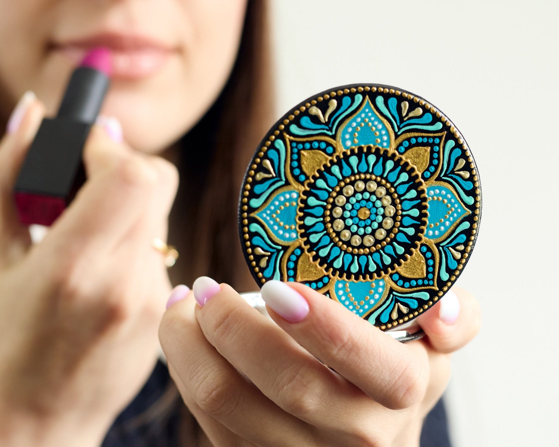 Woman making makeup looking in the compact mirror with turquoise blue mandala hand-painted design.
