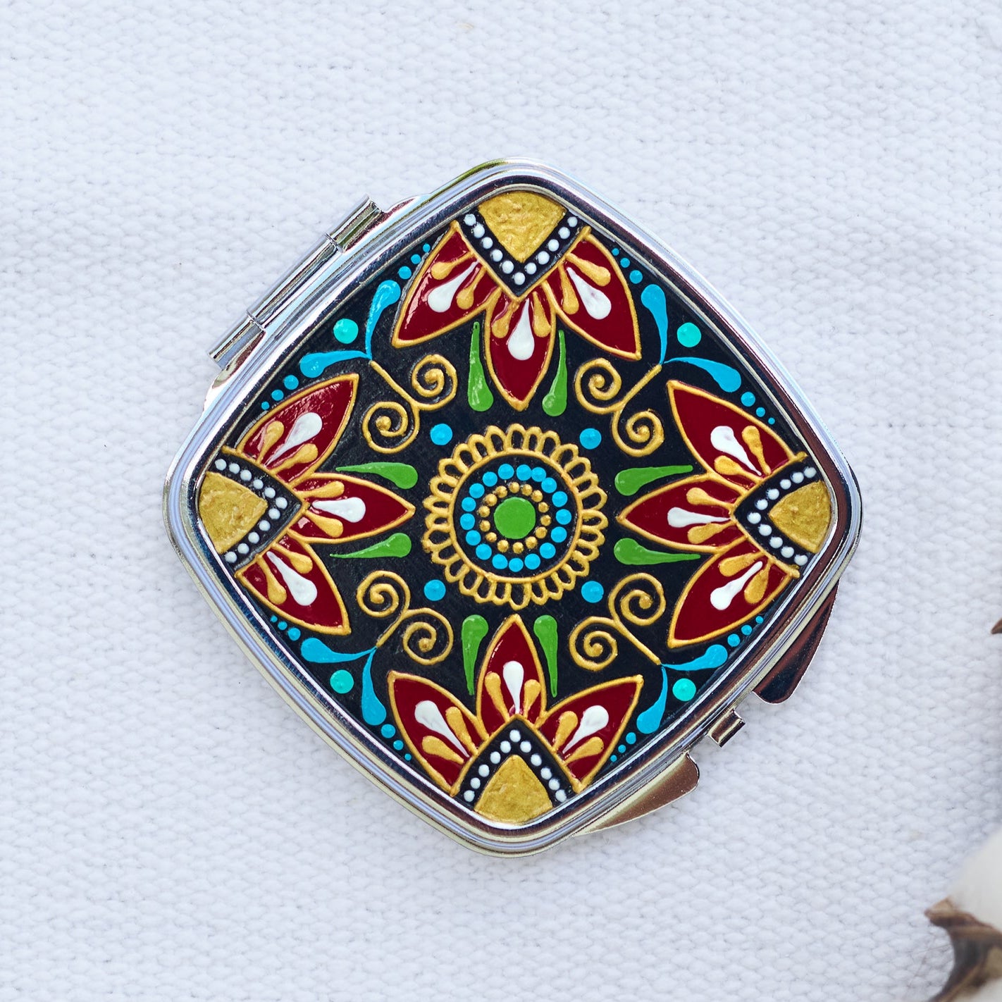 Compact pocket mirror with folk floral hand-painted design, top view on white background