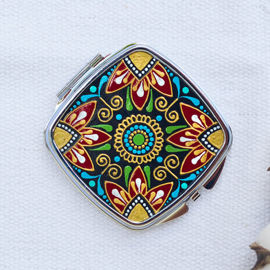 Compact pocket mirror with folk floral hand-painted design, top view on white background