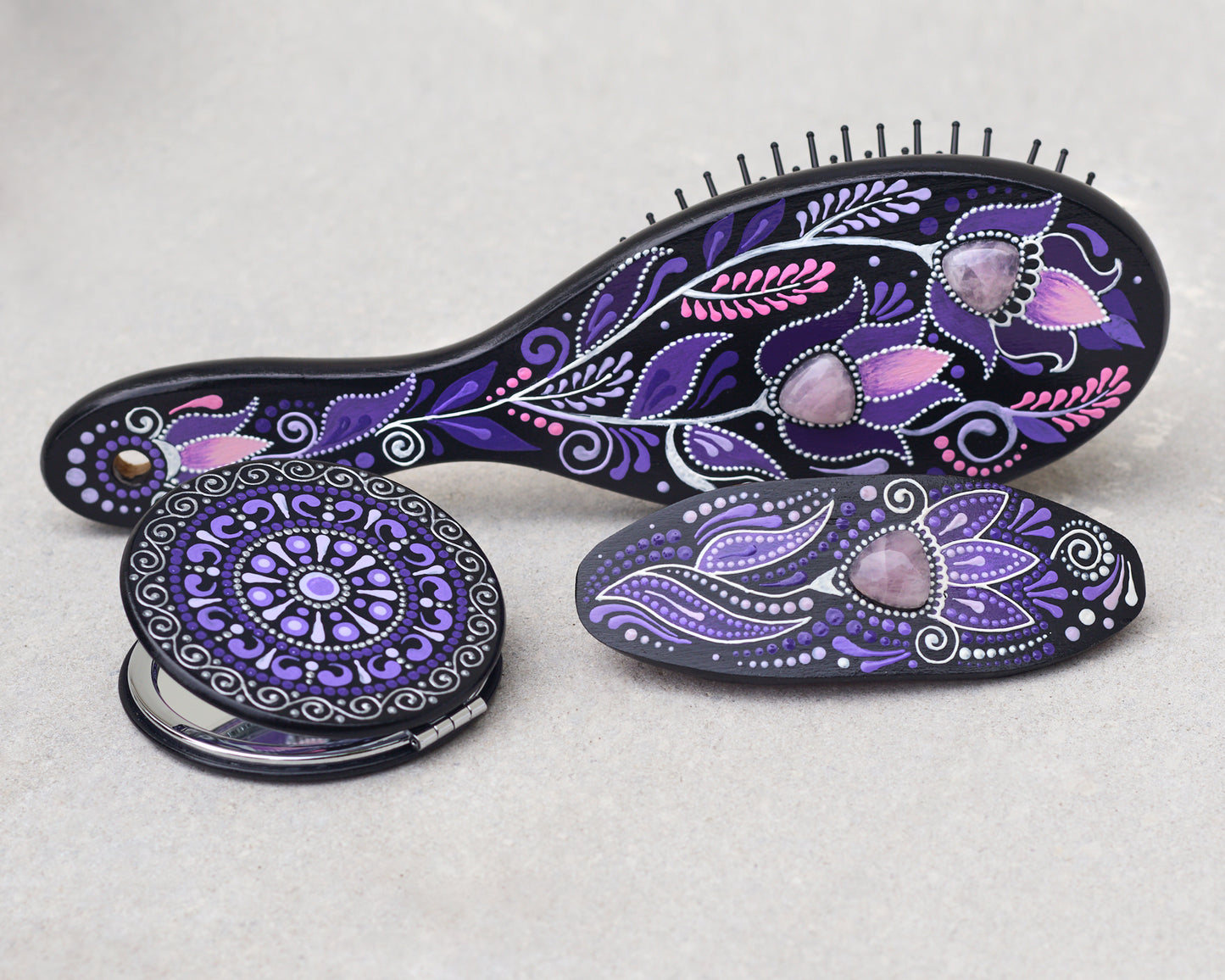 Purple hairbrush, mirror and barrette with purple and pink floral patterns on a light gray background