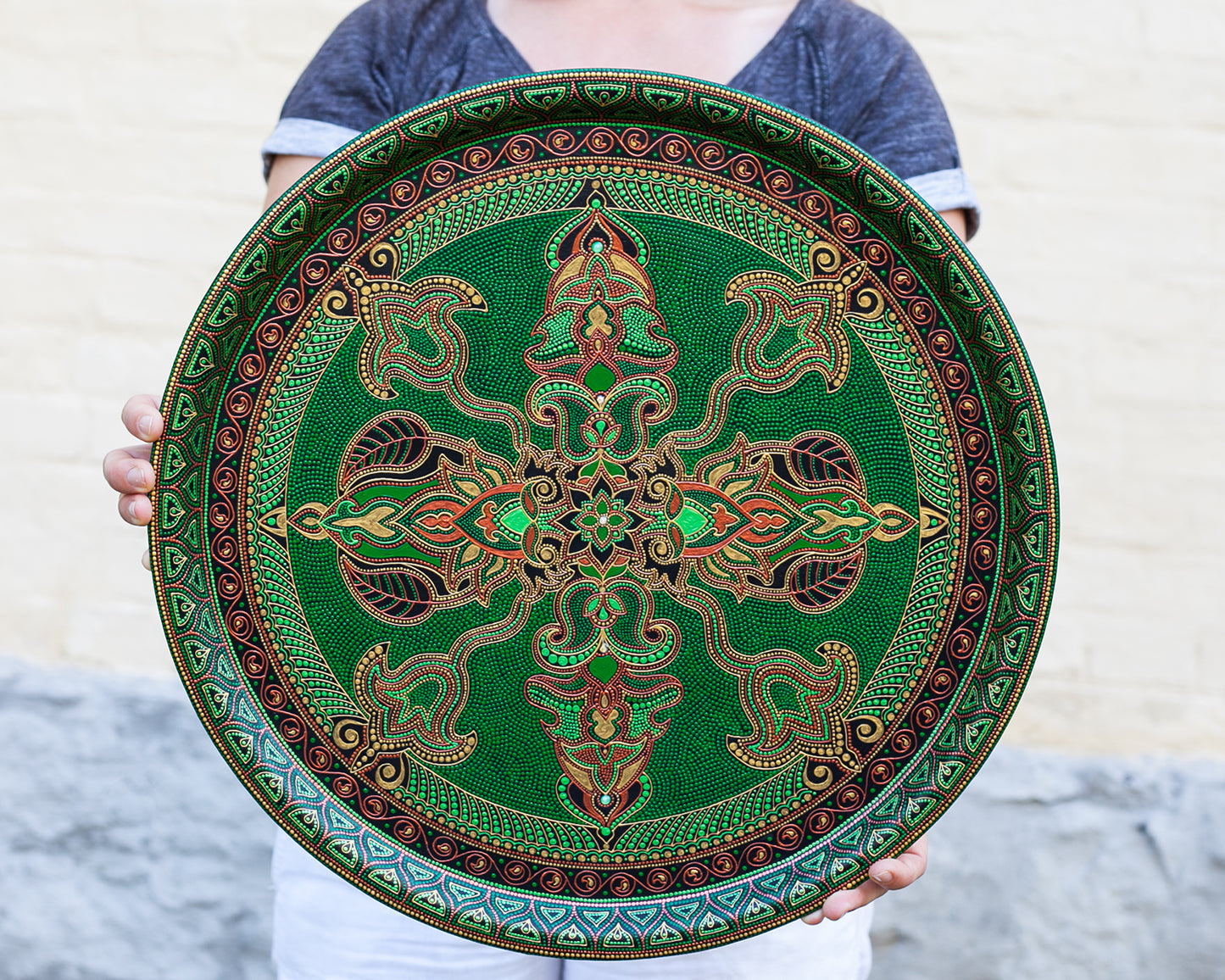 Woman holds in hands green hand-painted round metal tray, diameter 45 cm.